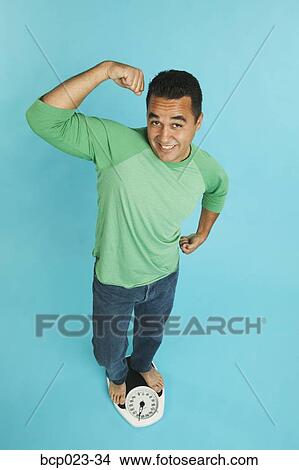 Man standing on scale and flexing his muscles View Large Photo Image Picture - Man standing on scale and flexing his muscles. Fotosearch