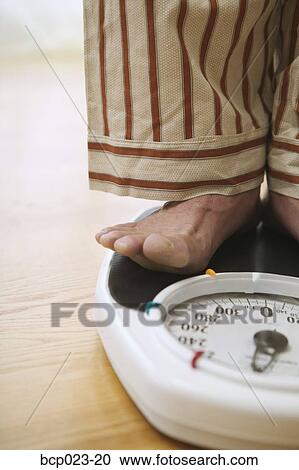 Stock Image - Man weighing himself on a bathroom scale. Fotosearch
