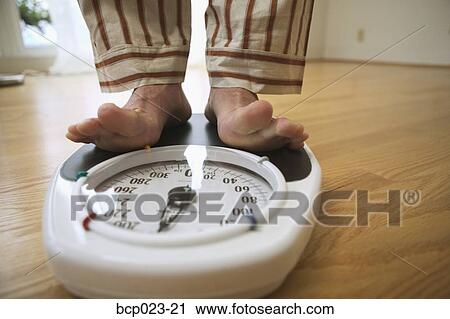 Stock Image - Man weighing himself on a bathroom scale. Fotosearch