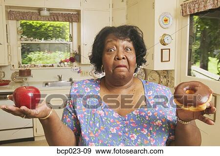 Woman deciding between an apple or a doughnut View Large Photo Image Stock Photo - Woman deciding between an apple or a doughnut. Fotosearch