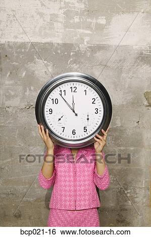 Woman holding a clock in front of her face View Large Photo Image Stock Photograph - Woman holding a clock in front of her face. Fotosearch