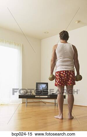 Stock Photography - A middle-age man lifting weights while watching TV. Fotosearch