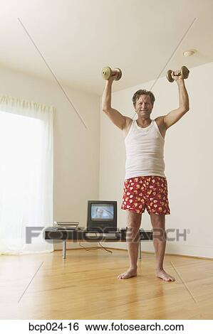 Middle-aged man lifting weights at home View Large Photo Image Stock Photograph - Middle-aged man lifting weights at home. Fotosearch
