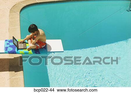 A boy sitting on a diving board with his laptop View Large Photo Image Picture - A boy sitting on a diving board with his laptop. Fotosearch