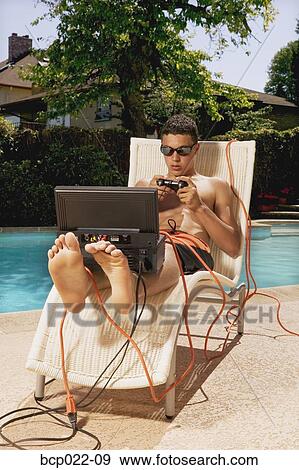 A teenaged boy playing video games poolside View Large Photo Image Stock Photo - A teenaged boy playing video games poolside. Fotosearch