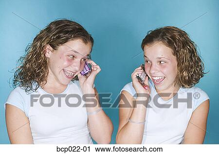 Stock Image - Teenaged twins with mobile phones. Fotosearch