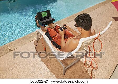 Stock Image - Teenager playing video games at poolside. Fotosearch
