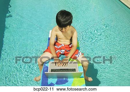 Youngster working on his laptop at poolside View Large Photo Image Stock Image - Youngster working on his laptop at poolside. Fotosearch