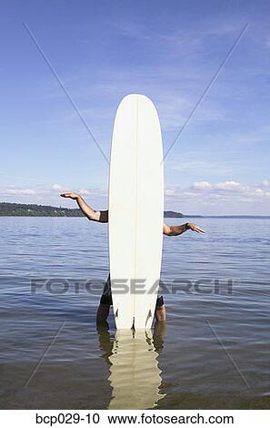 Stock Image - Man standing behind a surfboard. Fotosearch