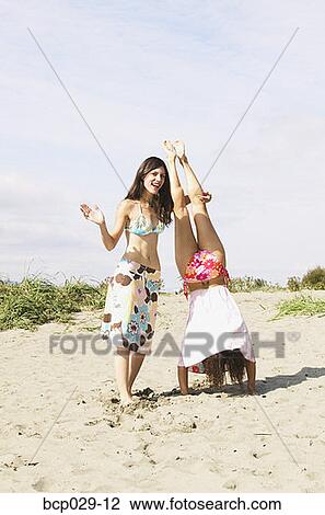 Stock Image - Woman helping her friend do a handstand. Fotosearch