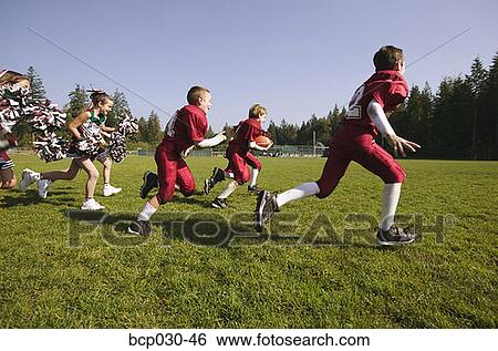 Stock Photograph - Players and cheerleaders running onto football field. Fotosearch