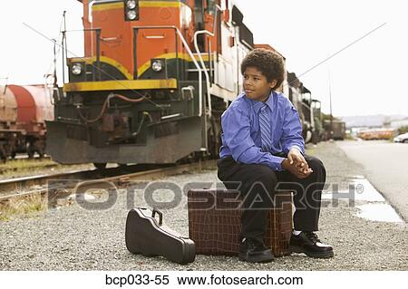 Stock Photography - Boy at train station sitting on suitcase. Fotosearch