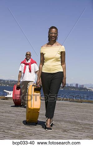Stock Image - Couple on dock pulling luggage. Fotosearch