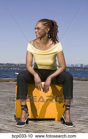 Stock Image - Woman outdoors sitting on suitcase. Fotosearch