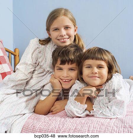 Stock Photo - Children sitting on bed wearing pajamas. Fotosearch