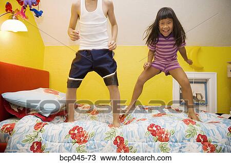 Stock Image - Girl and boy jumping bed. Fotosearch