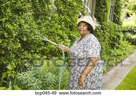 Woman watering her garden View Large Photo Image Stock Photo - Woman watering her garden. Fotosearch
