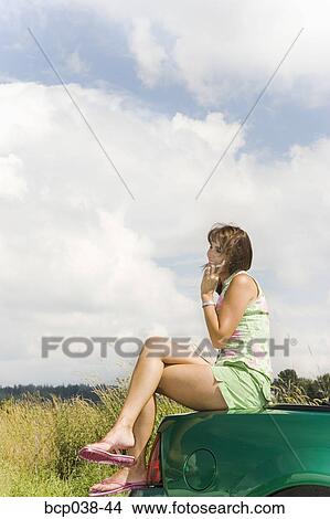 Woman sitting on car and talking on mobile phone View Large Photo Image Picture - Woman sitting on car and talking on mobile phone. Fotosearch