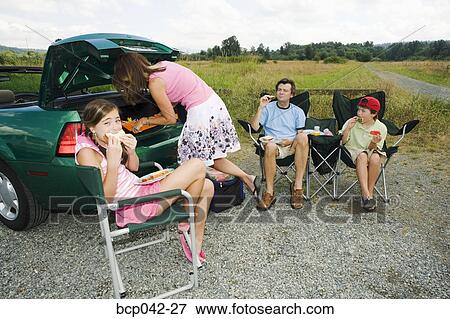 Family eating picnic lunch outside car View Large Photo Image Stock Photo - Family eating picnic lunch outside car. Fotosearch