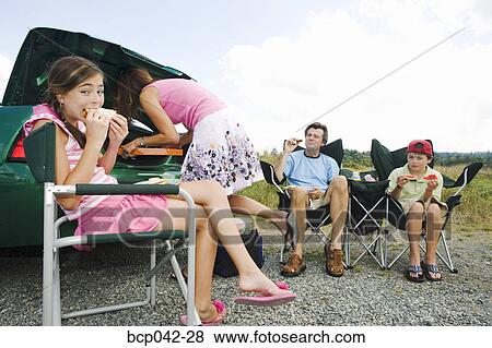 Stock Photo - Family eating picnic lunch outside car. Fotosearch
