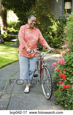 Smiling woman walking her bicycle View Large Photo Image Stock Photo - Smiling woman walking her bicycle. Fotosearch