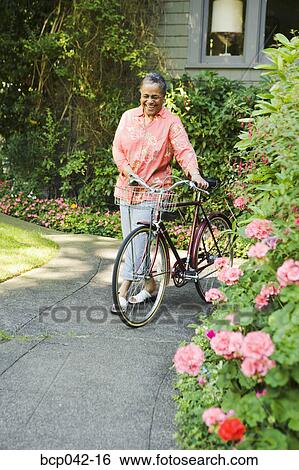 Smiling woman walking her bicycle View Large Photo Image Stock Photograph - Smiling woman walking her bicycle. Fotosearch