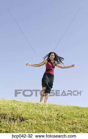 Stock Image - Young woman running on grassy hill. Fotosearch