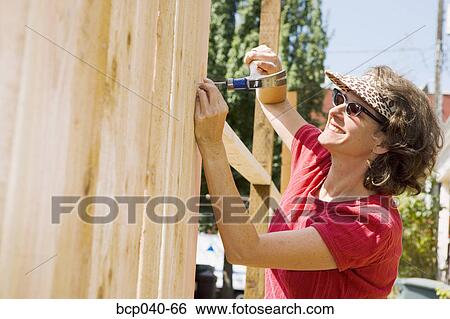 Stock Photograph - Smiling woman building fence. Fotosearch