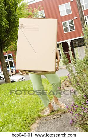 Stock Image - Woman carrying a heavy box. Fotosearch