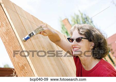 Woman hammering wooden fence View Large Photo Image Stock Photo - Woman hammering wooden fence. Fotosearch