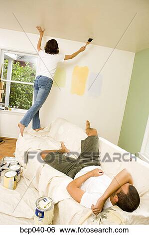 Stock Photograph - Woman painting walls while man rests. Fotosearch