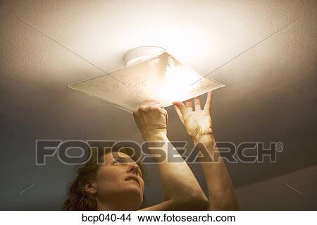Picture - Woman repairing lighting fixture on ceiling. Fotosearch