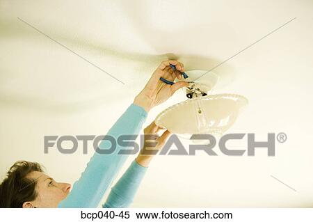 Stock Photography - Woman repairing lighting fixture on ceiling. Fotosearch