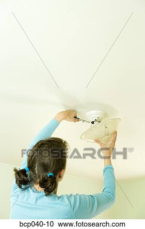 Stock Image - Woman with pigtails repairing light fixture. Fotosearch