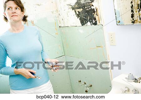 Stock Image - Woman with plumbing fixtures in bathroom. Fotosearch