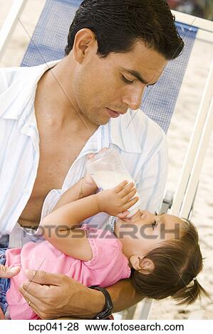 Stock Photo - Dad holding daughter drinking from bottle. Fotosearch