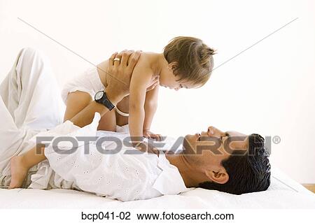 Dad lying on bed holding toddler View Large Photo Image Stock Image - Dad lying on bed holding toddler. Fotosearch