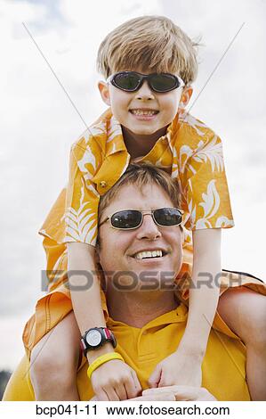 Stock Image - Little boy riding on dad's shoulders. Fotosearch