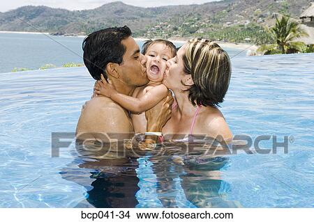 Picture - Parents kissing toddler in tropical pool. Fotosearch