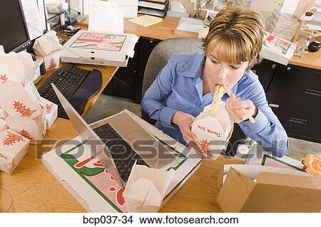 Picture - Office worker eating at her desk. Fotosearch