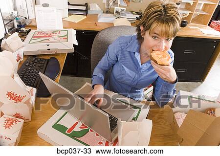 Stock Image - Office worker eating at her desk. Fotosearch
