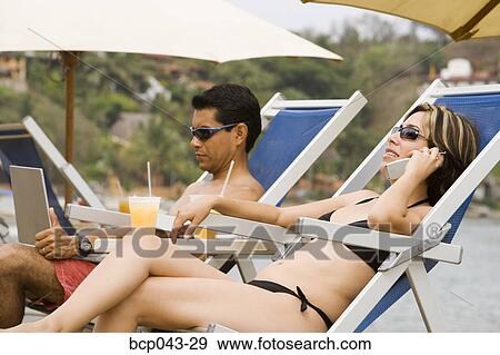 Couple using laptop and phone at beach View Large Photo Image Stock Photo - Couple using laptop and phone at beach. Fotosearch