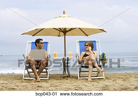 Couple using laptop and phone on beach View Large Photo Image Stock Image - Couple using laptop and phone on beach. Fotosearch