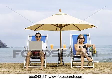 Couple using laptop and phone on beach View Large Photo Image Stock Photo - Couple using laptop and phone on beach. Fotosearch