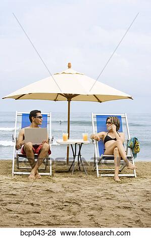 Stock Photo - Couple using laptop and phone on beach. Fotosearch