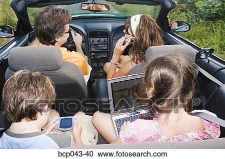 Stock Image - Family in convertible using portable electronics. Fotosearch