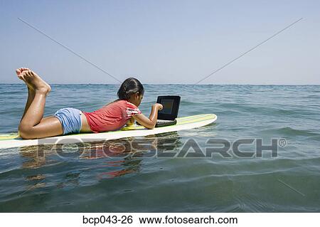 Girl using laptop while floating on surfboard View Large Photo Image Stock Photograph - Girl using laptop while floating on surfboard. Fotosearch