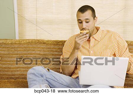 Man eating muffin and using laptop View Large Photo Image Stock Photo - Man eating muffin and using laptop. Fotosearch