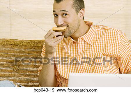 Man eating muffin and using laptop View Large Photo Image Stock Photo - Man eating muffin and using laptop. Fotosearch