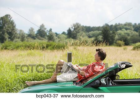 Stock Photo - Man on car hood using laptop. Fotosearch